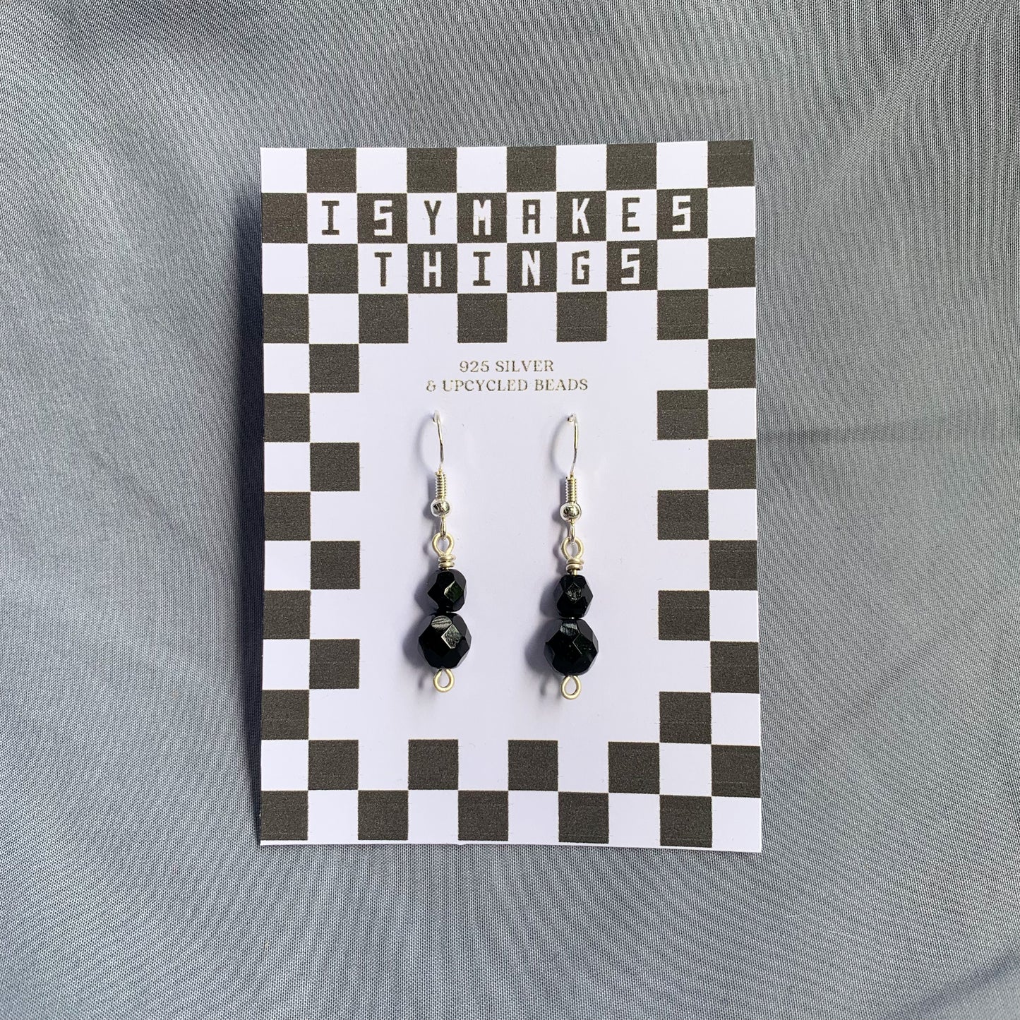 Black gem earrings on a checkerboard backing against a blue background