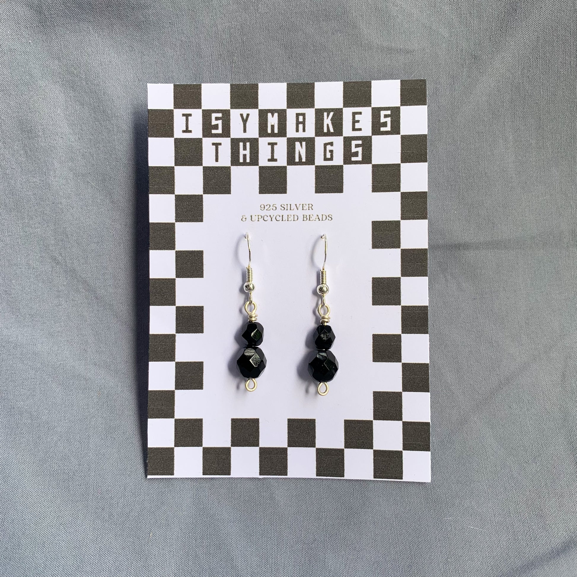 Black gem earrings on a checkerboard backing against a blue background