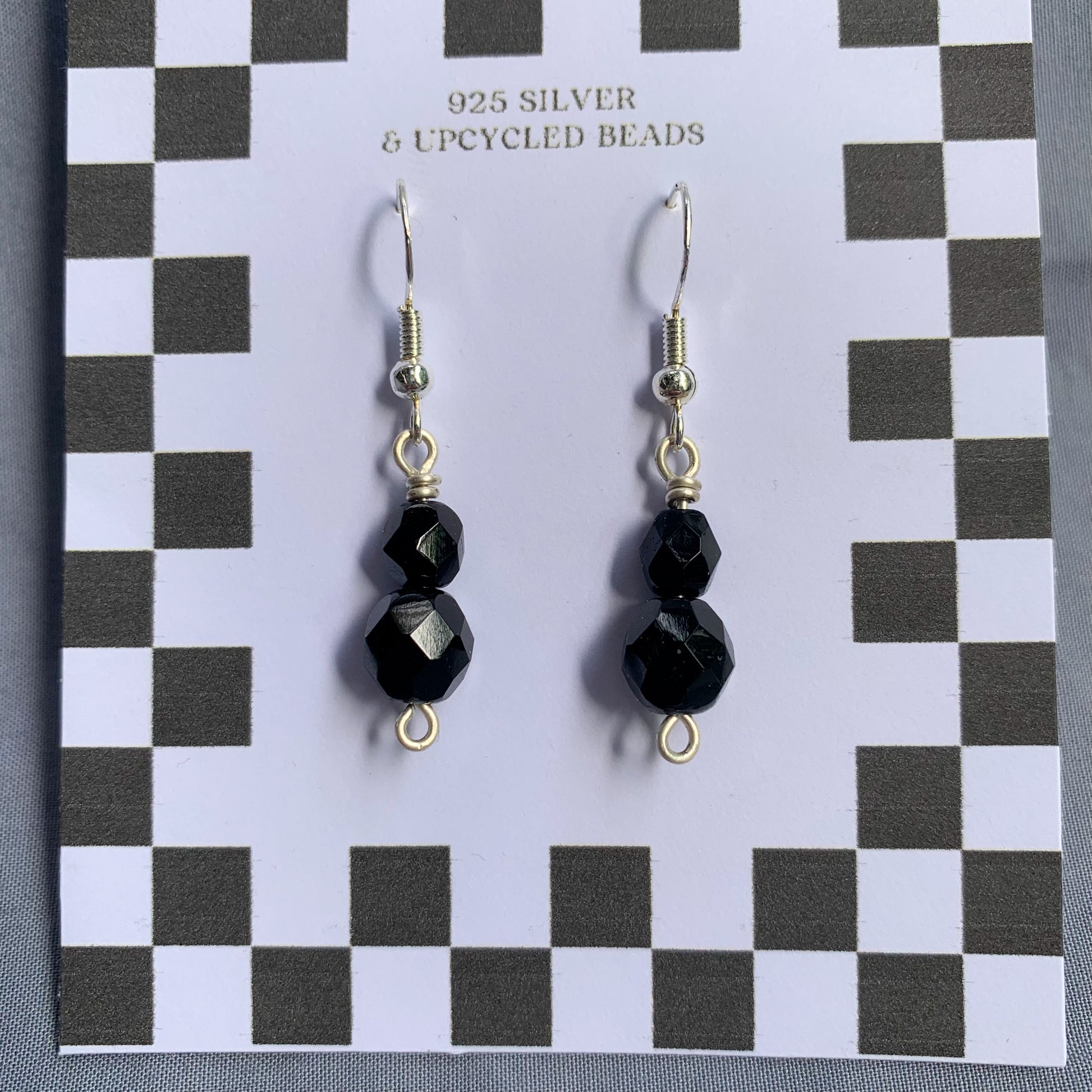 Black gem earrings on a checkerboard backing against a blue background