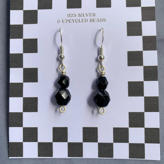 Black gem earrings on a checkerboard backing against a blue background