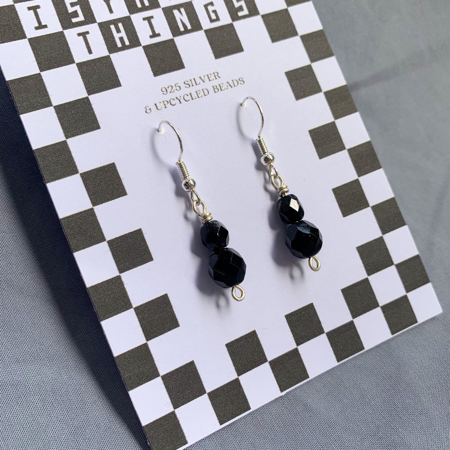 Black gem earrings on a checkerboard backing against a blue background