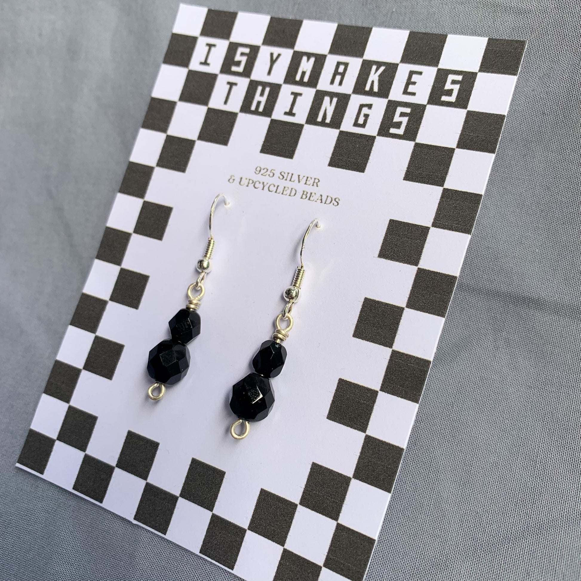 Black gem earrings on a checkerboard backing against a blue background