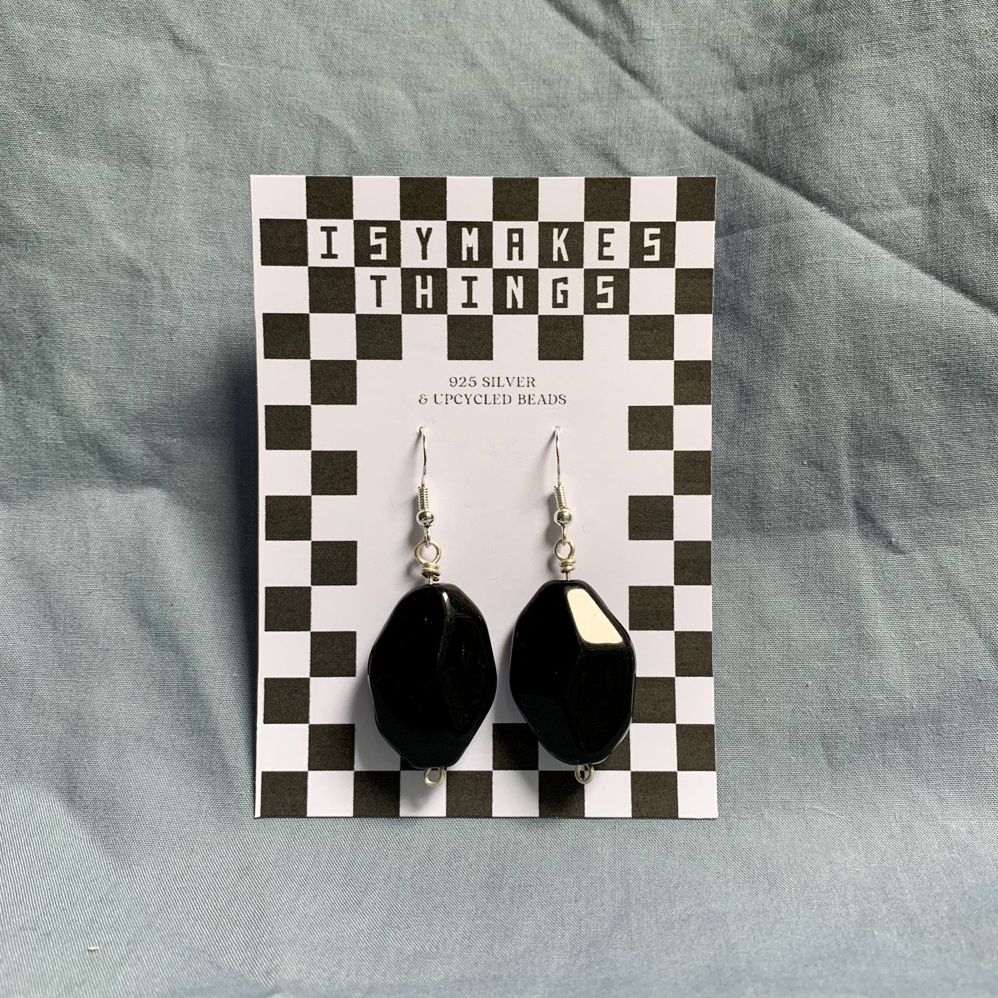 large black diamond shaped earrings hang off a white and black checkerboard backing card