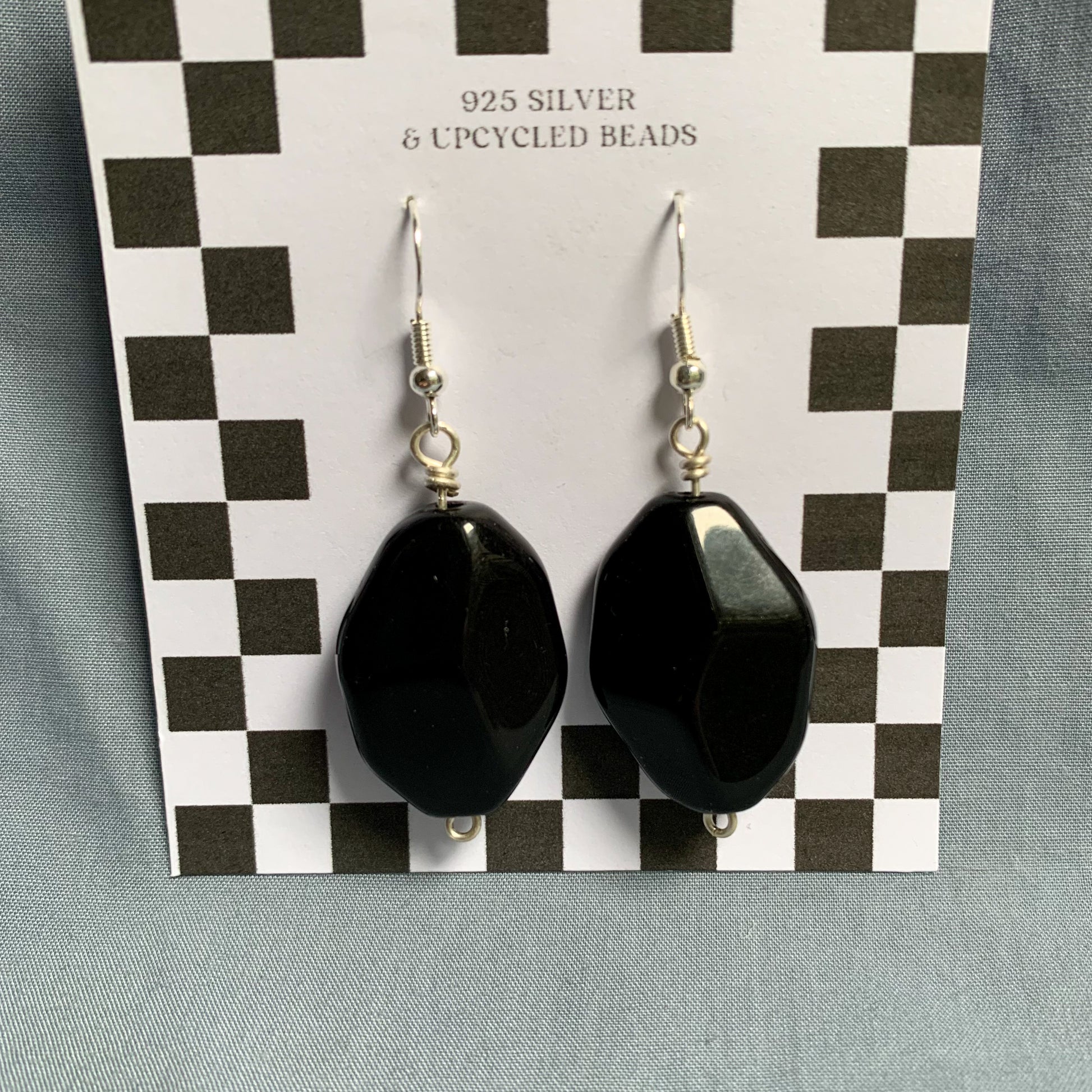 large black diamond shaped earrings hang off a white and black checkerboard backing card