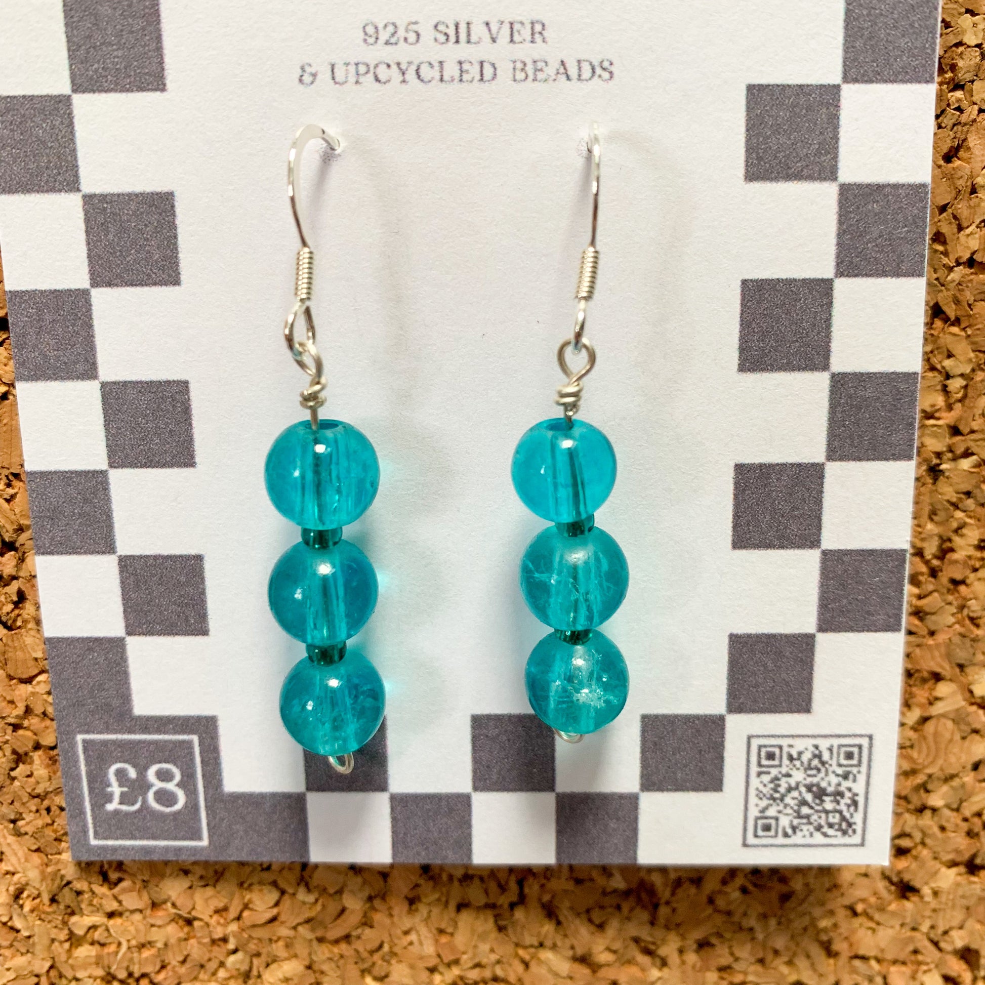blue bead earrings on a checkerboard backing pegged to a corkboard against a blue background