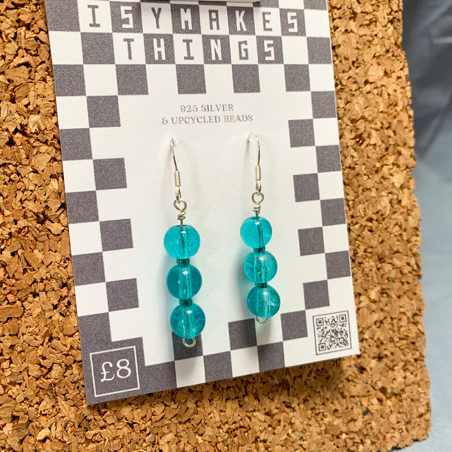 blue bead earrings on a checkerboard backing pegged to a corkboard against a blue background