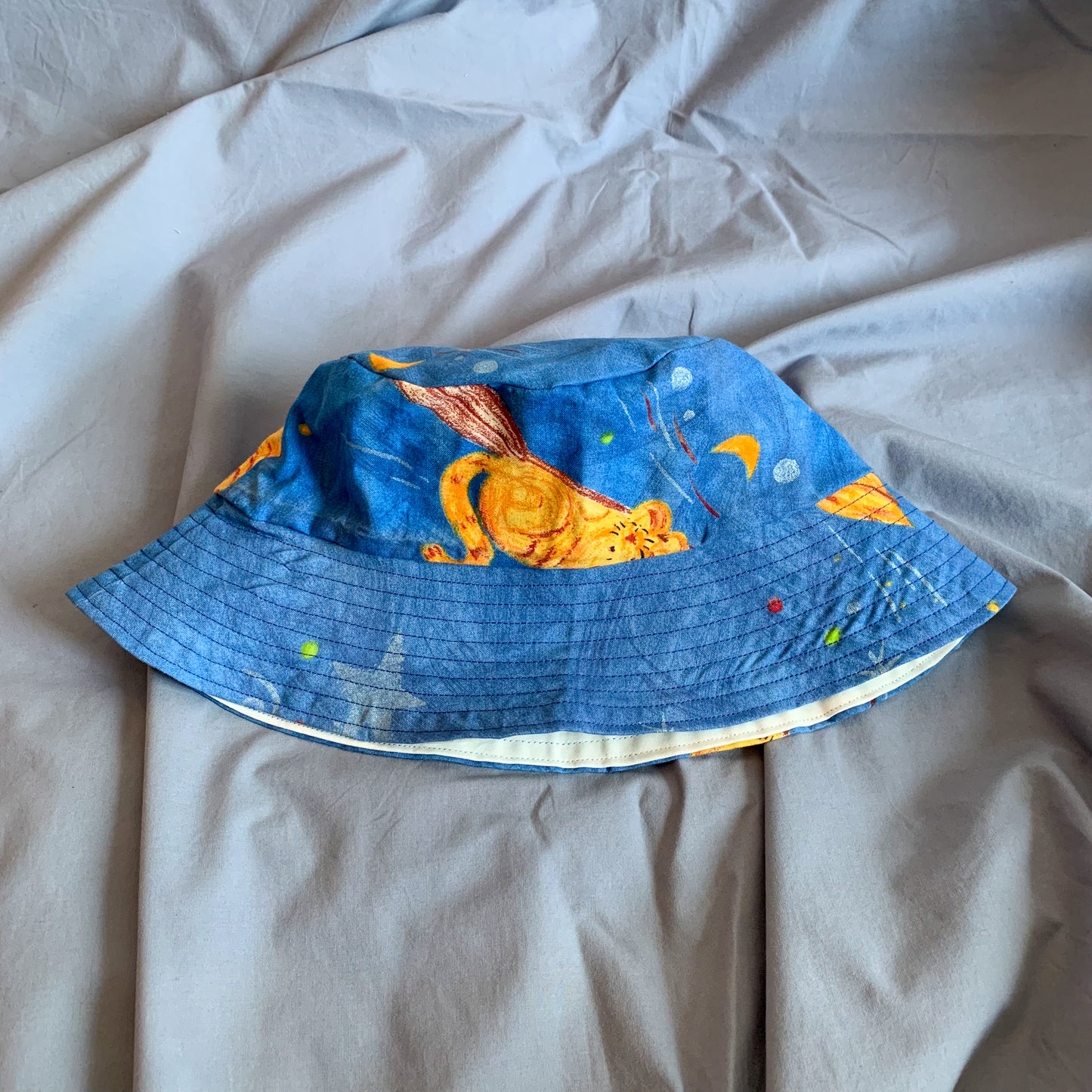 A blue bucket hat with part of a cartoon cat folded in half sat on a blue background