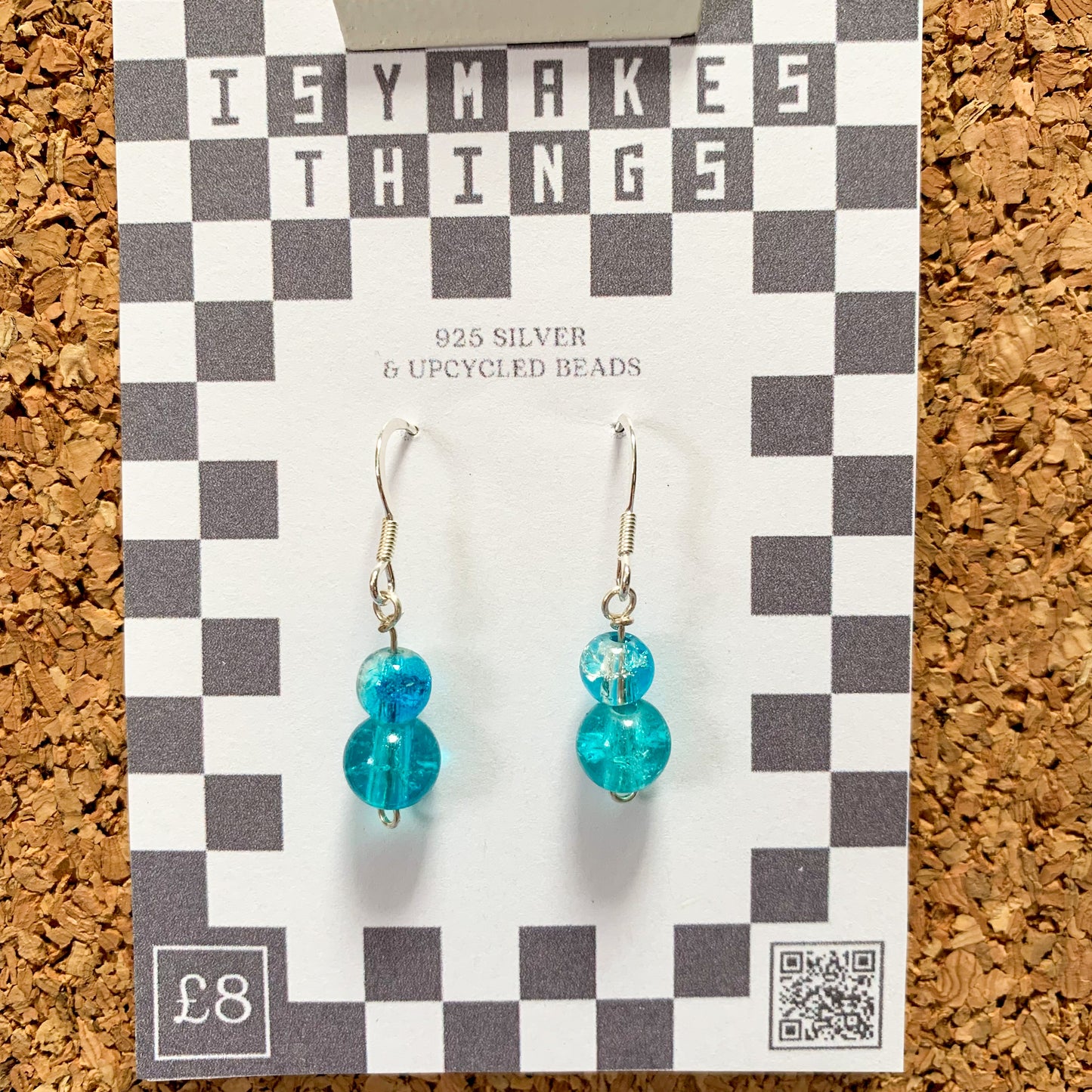 blue bead earrings on a checkerboard backing pegged to a corkboard against a blue background