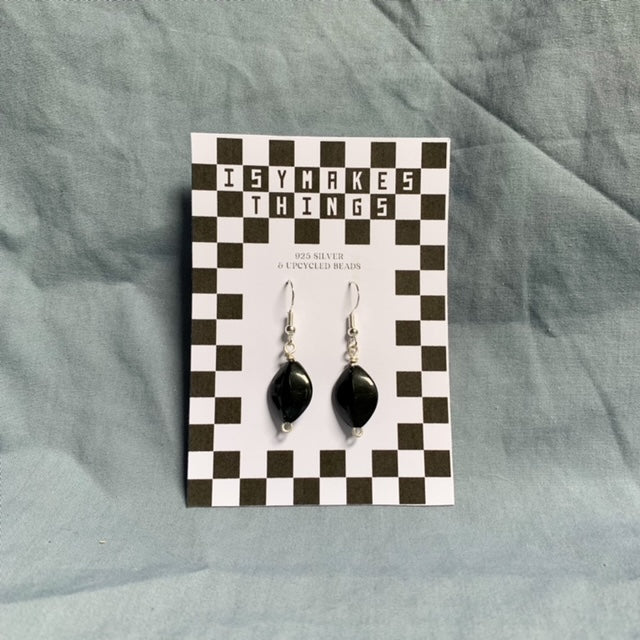 Black diamond shaped earrings hang off a checkered backing card with the title isymakesthings