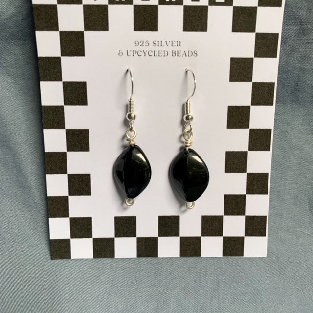 Black diamond shaped earrings hang off a checkered backing card with the title isymakesthings