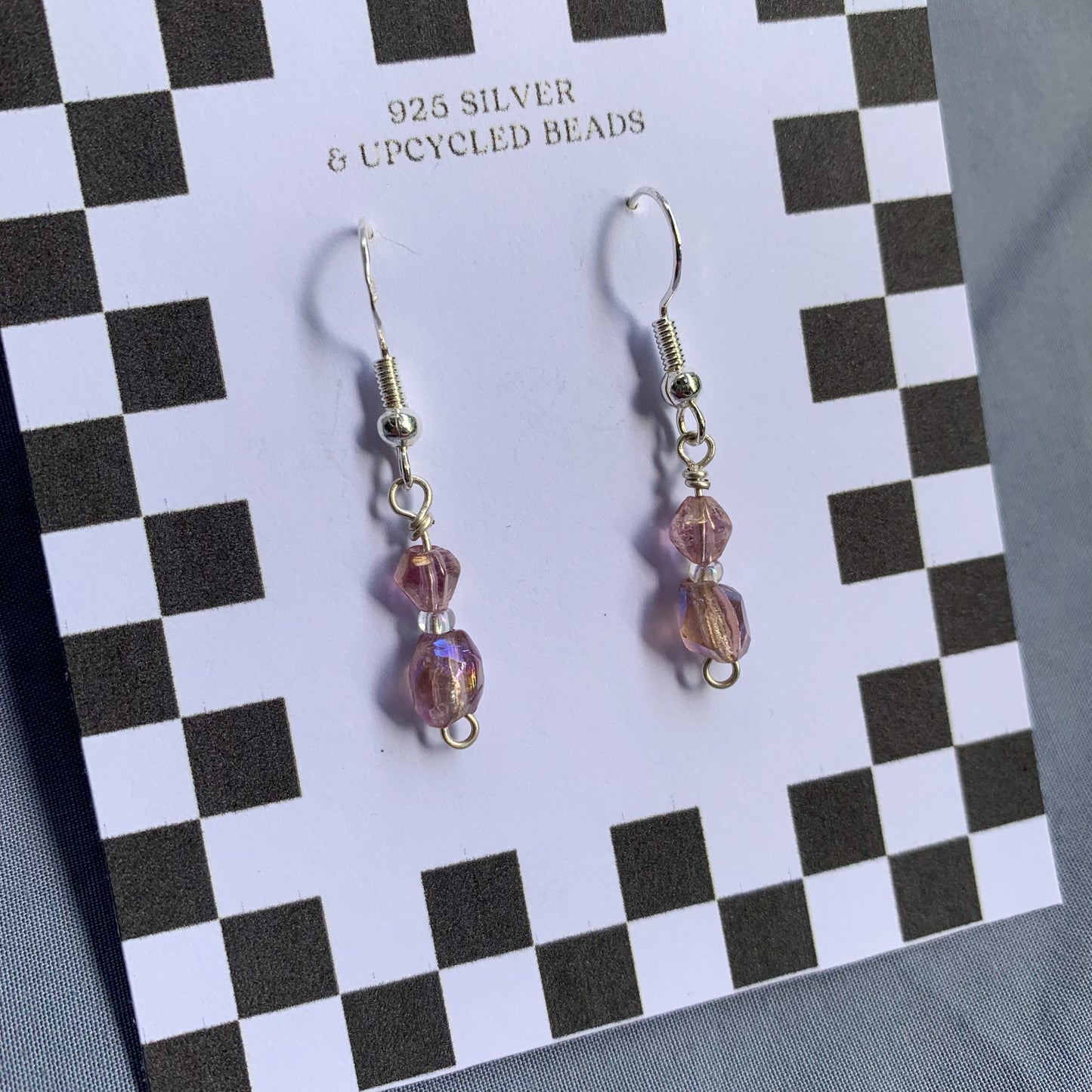 Purple gem earrings on a checkerboard backing against a blue background