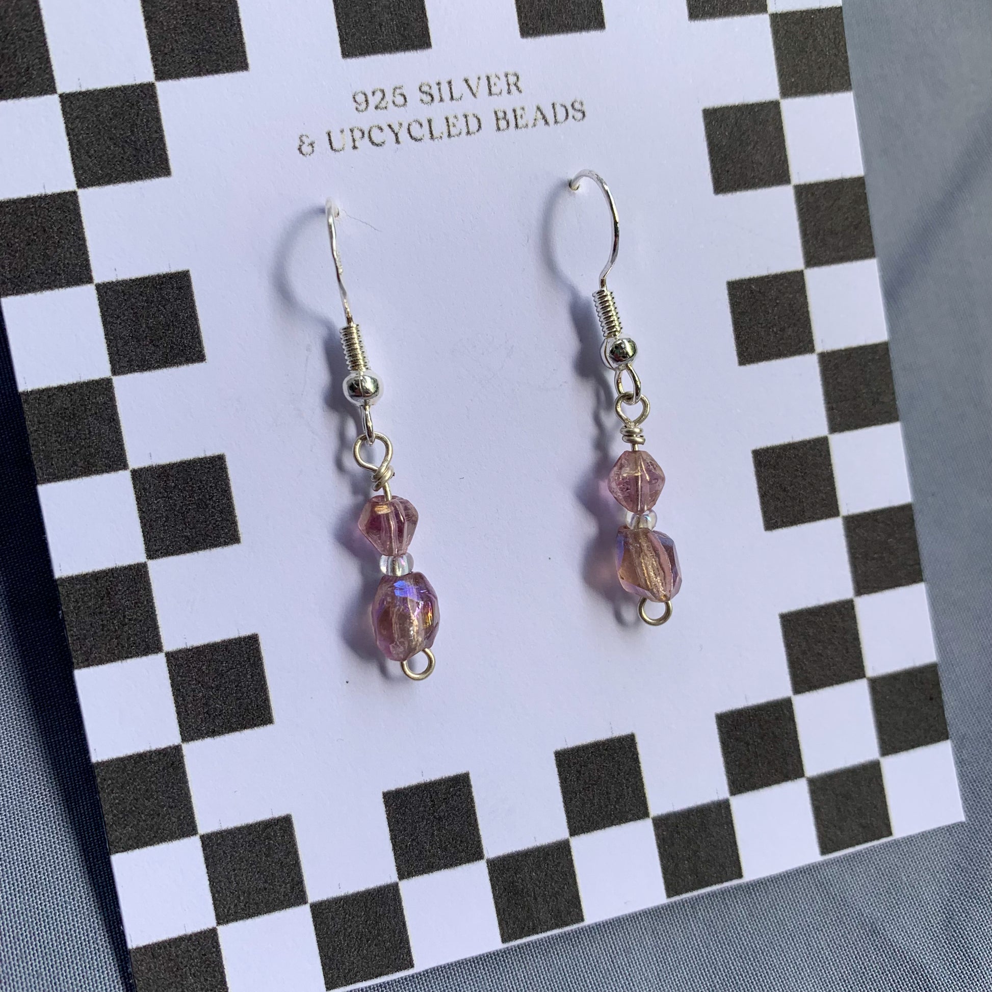 Purple gem earrings on a checkerboard backing against a blue background