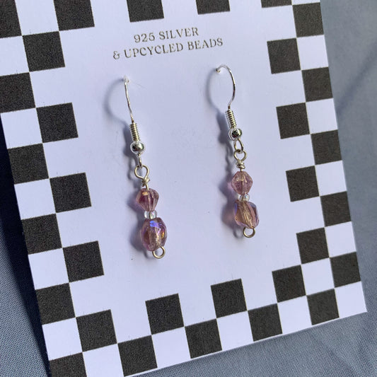 Purple gem earrings on a checkerboard backing against a blue background
