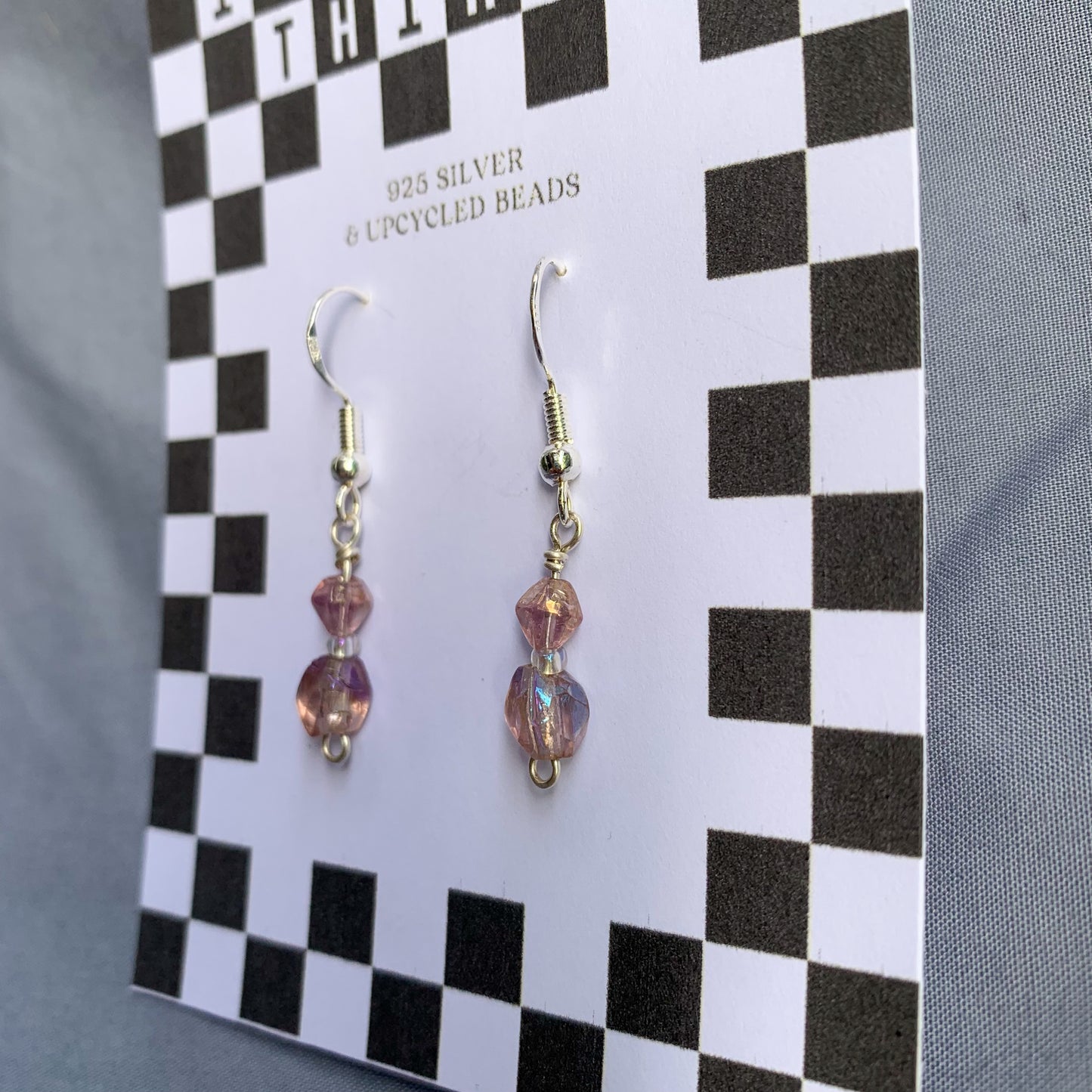 Purple gem earrings on a checkerboard backing against a blue background