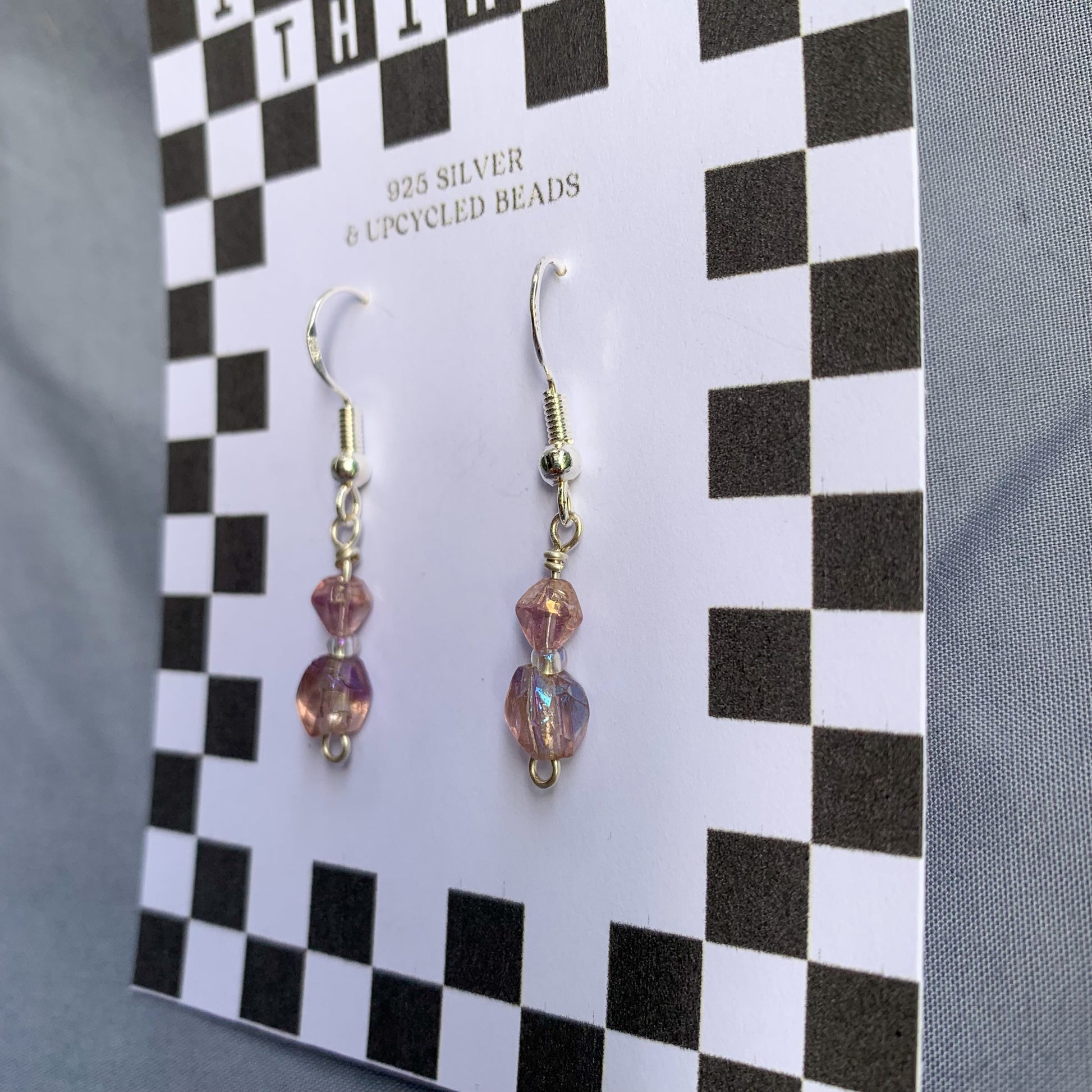 Purple gem earrings on a checkerboard backing against a blue background