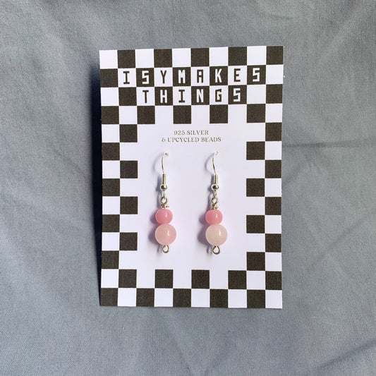 A darker pink ball stacked on top of a lighter pink ball earrings on a checkerboard backing against a blue background