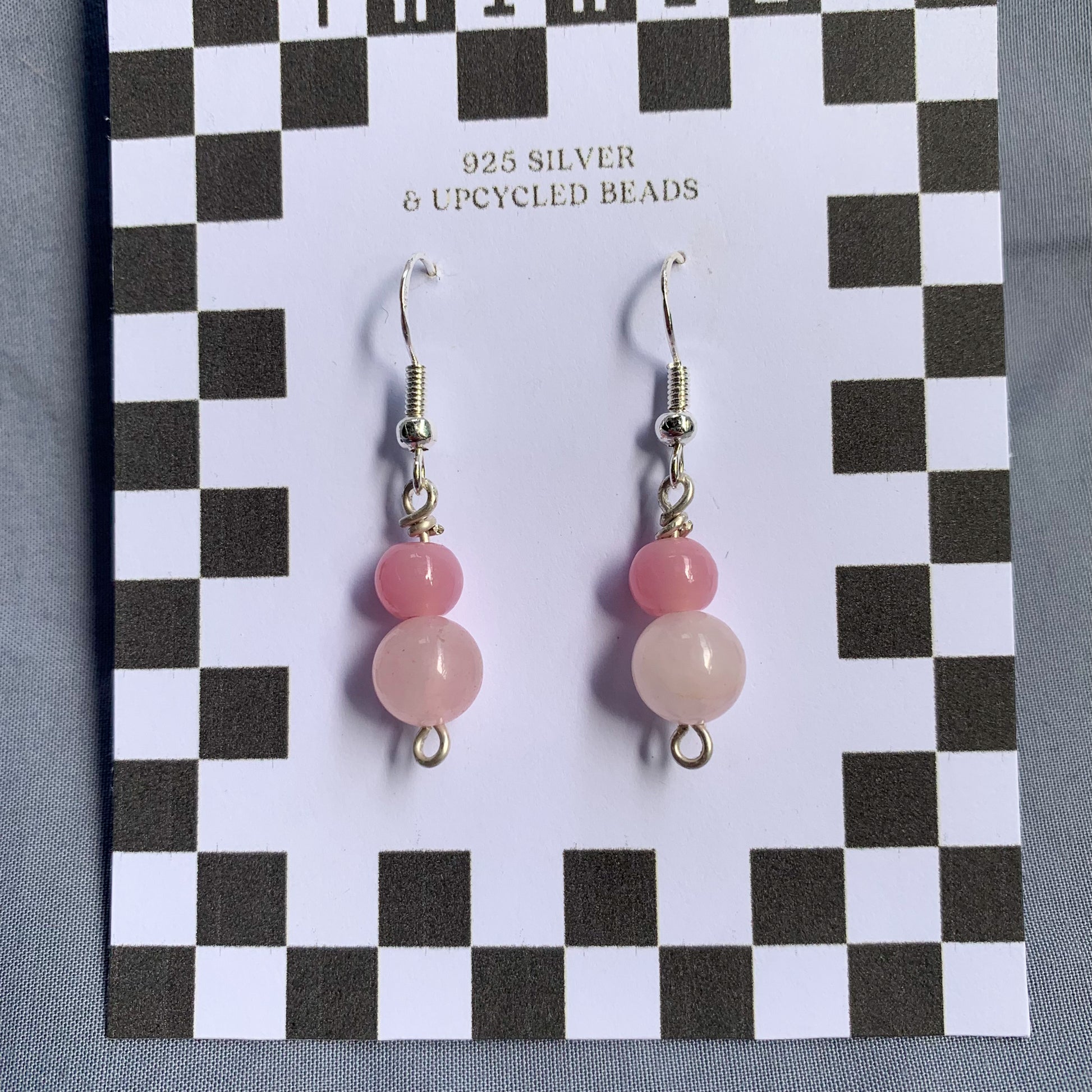 A darker pink ball stacked on top of a lighter pink ball earrings on a checkerboard backing against a blue background