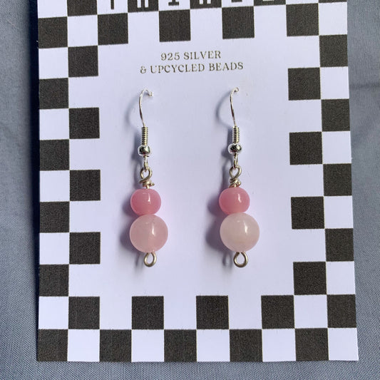 A darker pink ball stacked on top of a lighter pink ball earrings on a checkerboard backing against a blue background