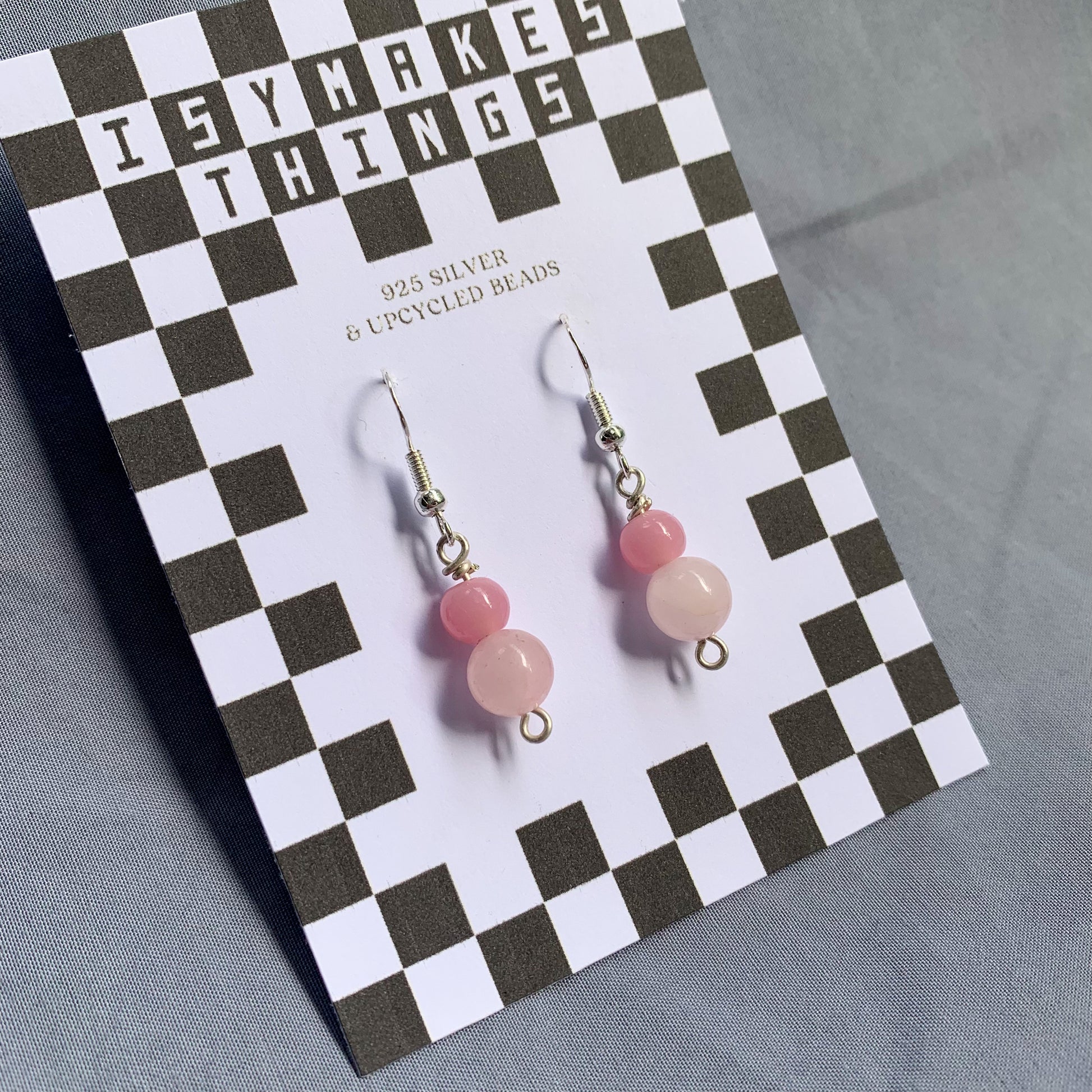 A darker pink ball stacked on top of a lighter pink ball earrings on a checkerboard backing against a blue background