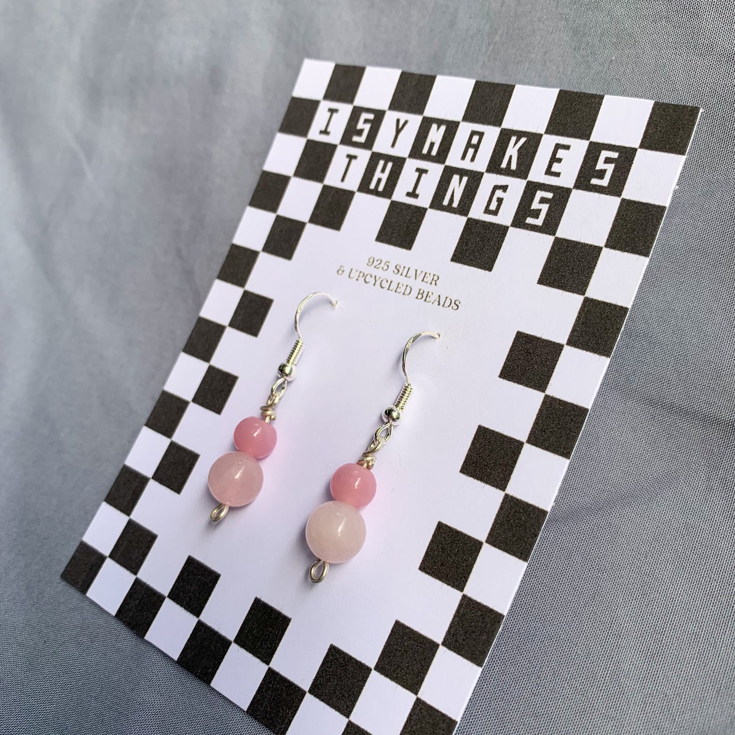 A darker pink ball stacked on top of a lighter pink ball earrings on a checkerboard backing against a blue background