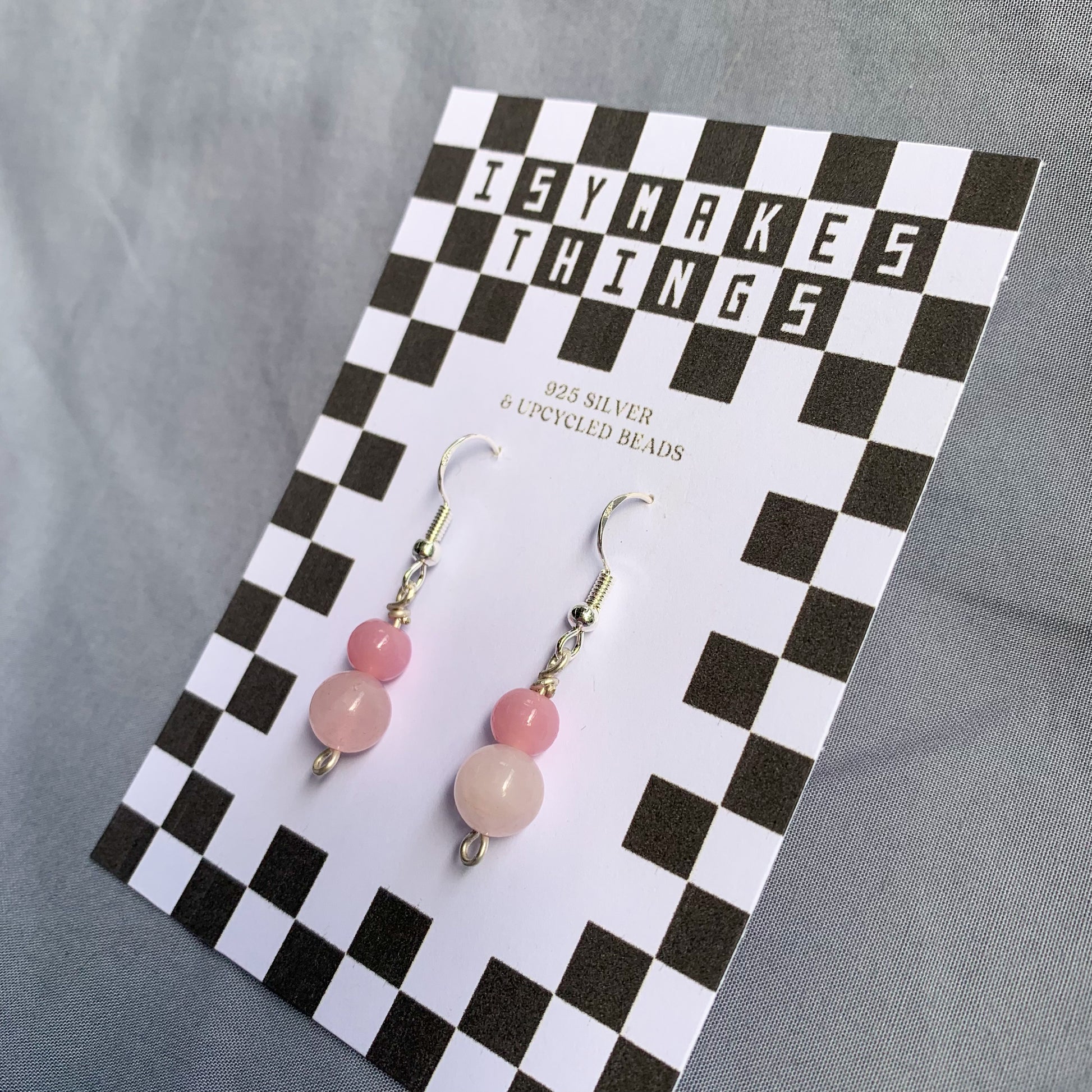 A darker pink ball stacked on top of a lighter pink ball earrings on a checkerboard backing against a blue background