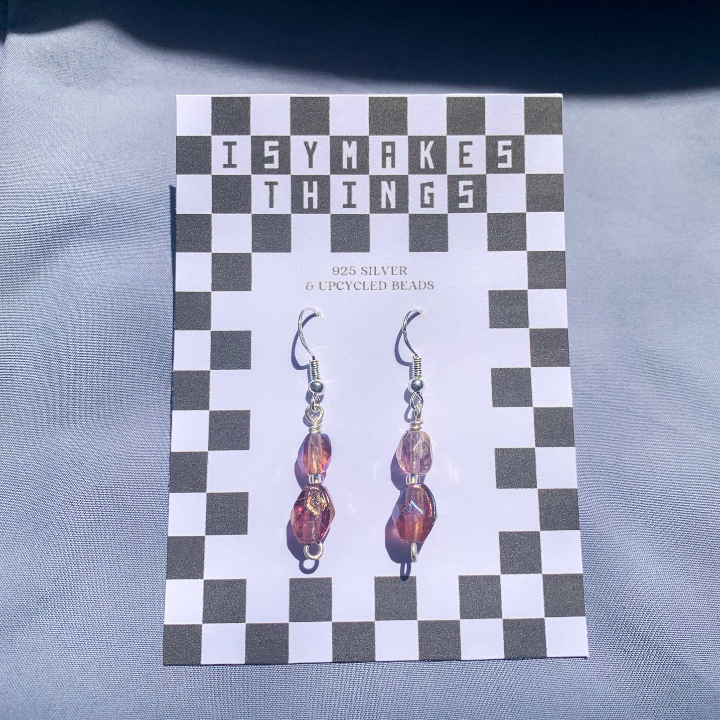 Purple gem earrings on a checkerboard backing against a blue background