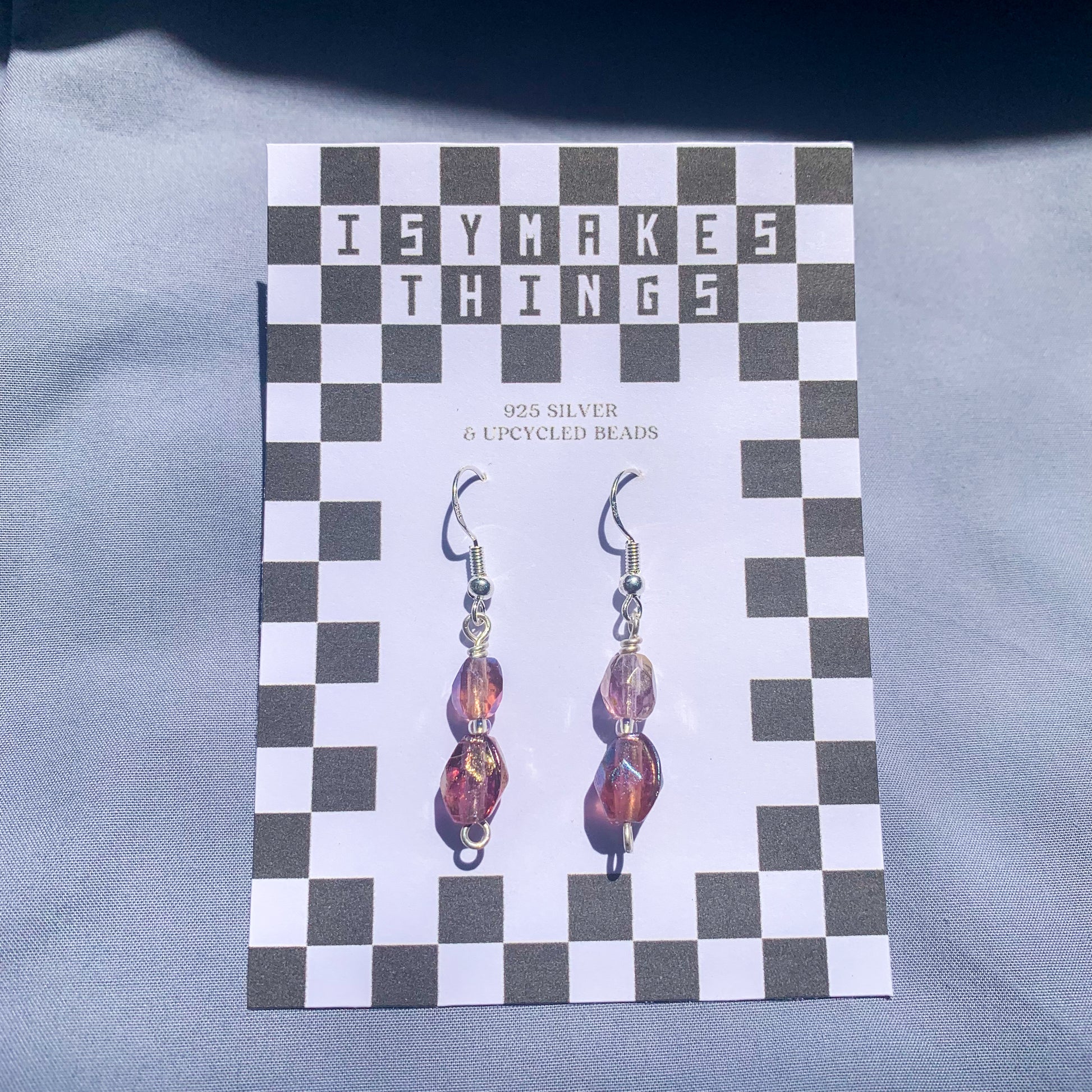 Purple gem earrings on a checkerboard backing against a blue background