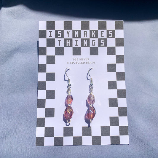 Purple gem earrings on a checkerboard backing against a blue background