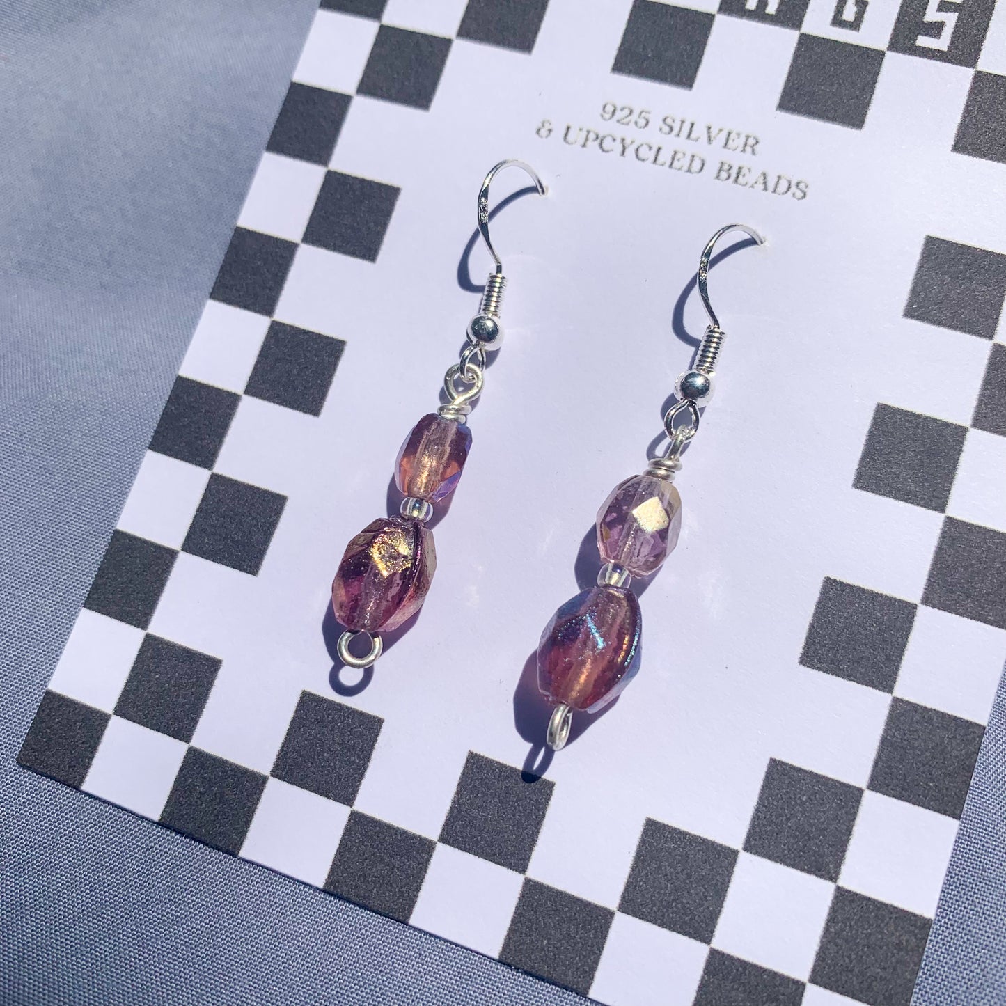 Purple gem earrings on a checkerboard backing against a blue background