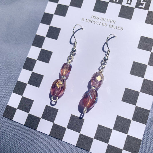 Purple gem earrings on a checkerboard backing against a blue background