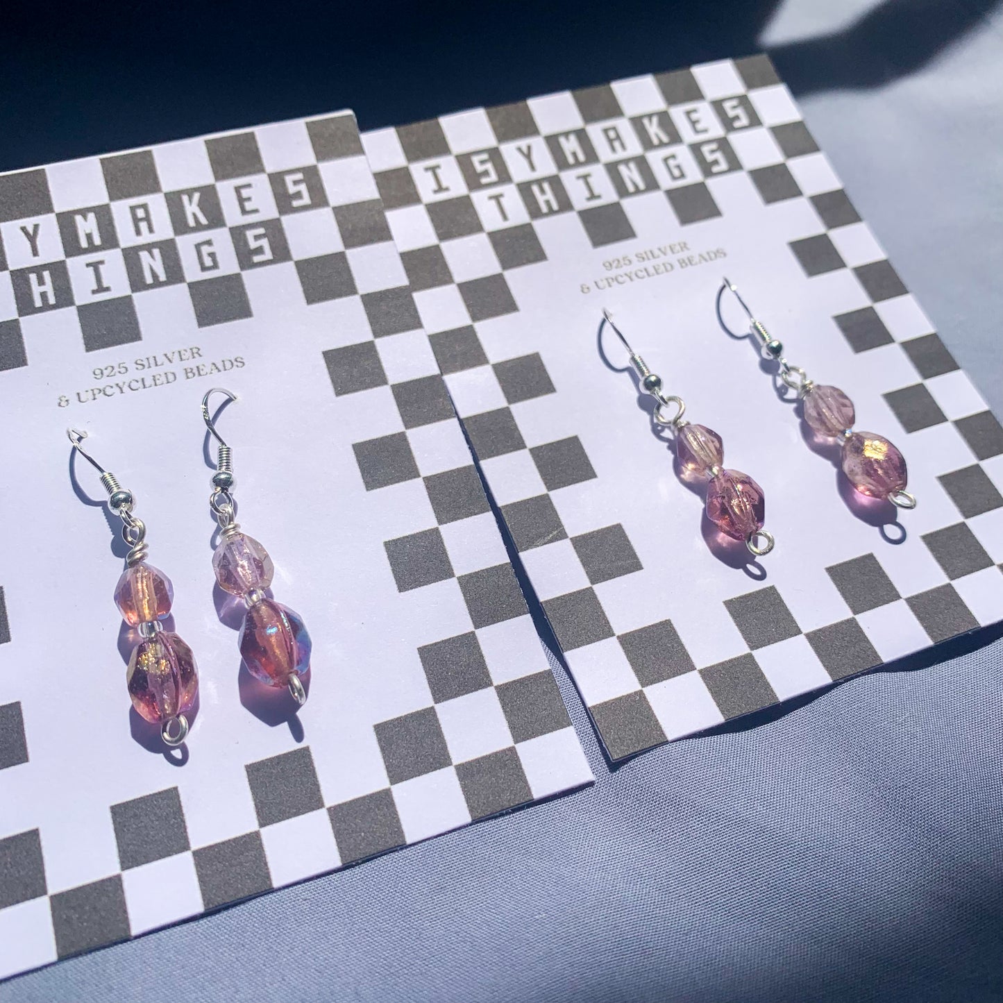 Purple gem earrings on a checkerboard backing against a blue background