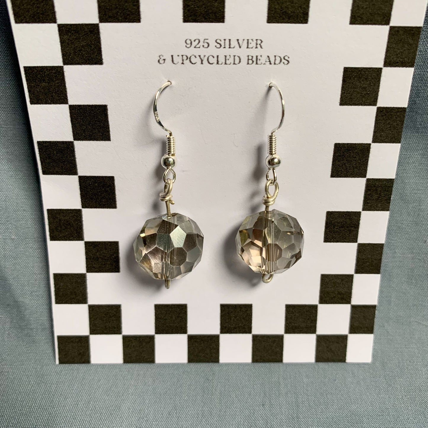 Shiny geometric clear ball earrings hang off a black and white checkered backing card with the title isymakesthings