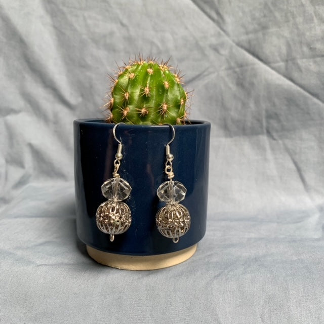 Shiny ball stacked earrings hang off a dark blue cactus pot