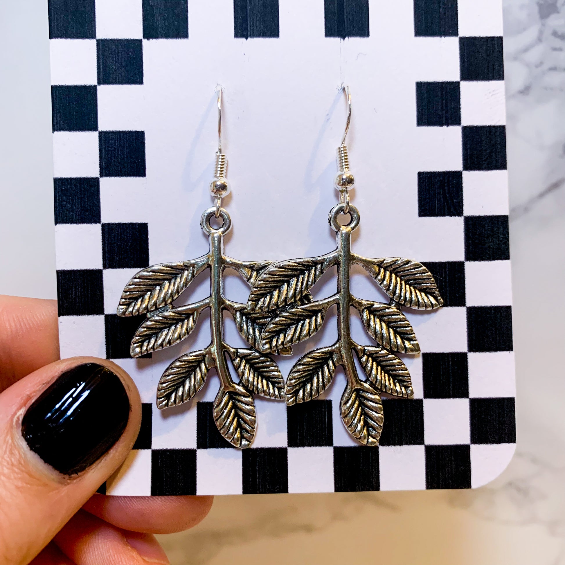 Silver leaf dangle earrings on a black and white checkered backing card with the title isymakesthings