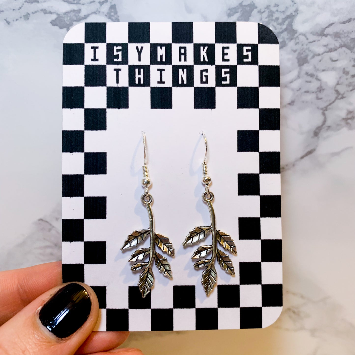 Silver leaf dangle earrings on a black and white checkered backing card with the title isymakesthings