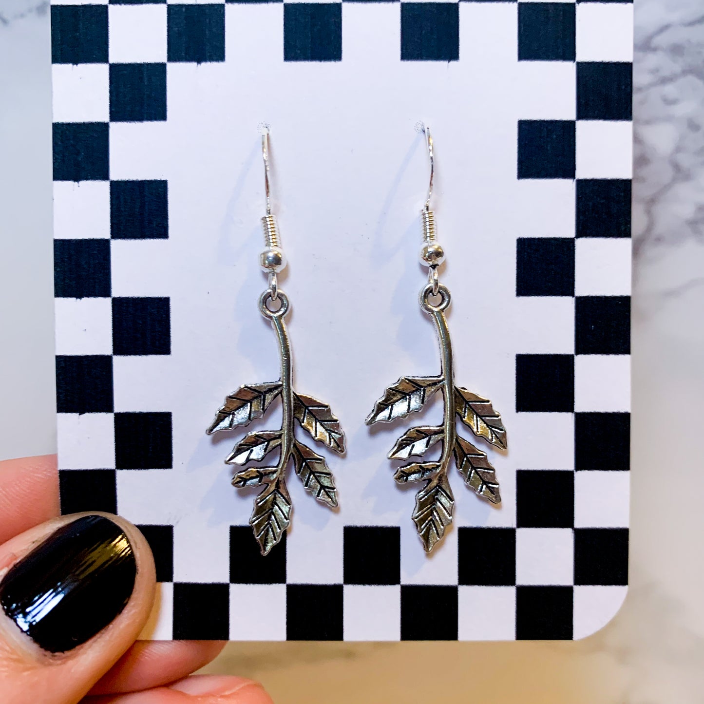 Silver leaf dangle earrings on a black and white checkered backing card with the title isymakesthings