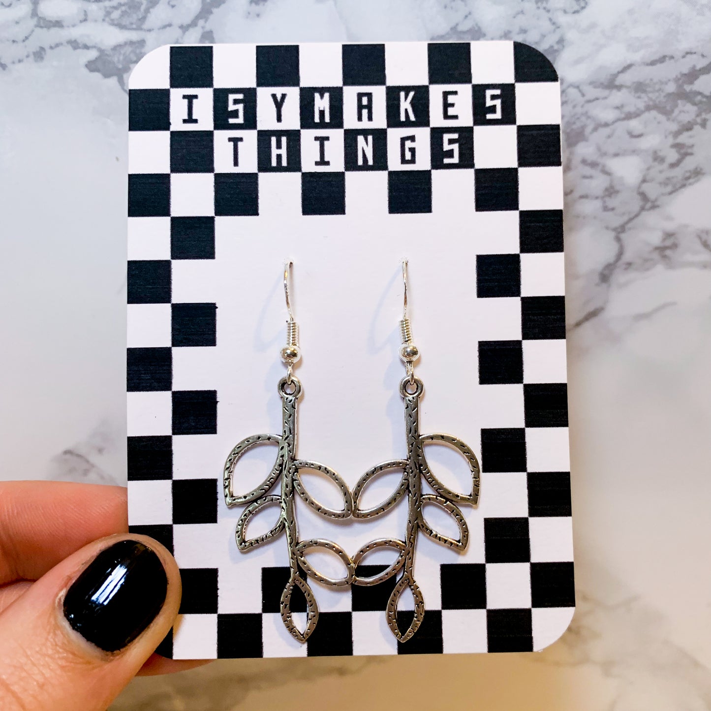 Silver leaf dangle earrings on a black and white checkered backing card with the title isymakesthings