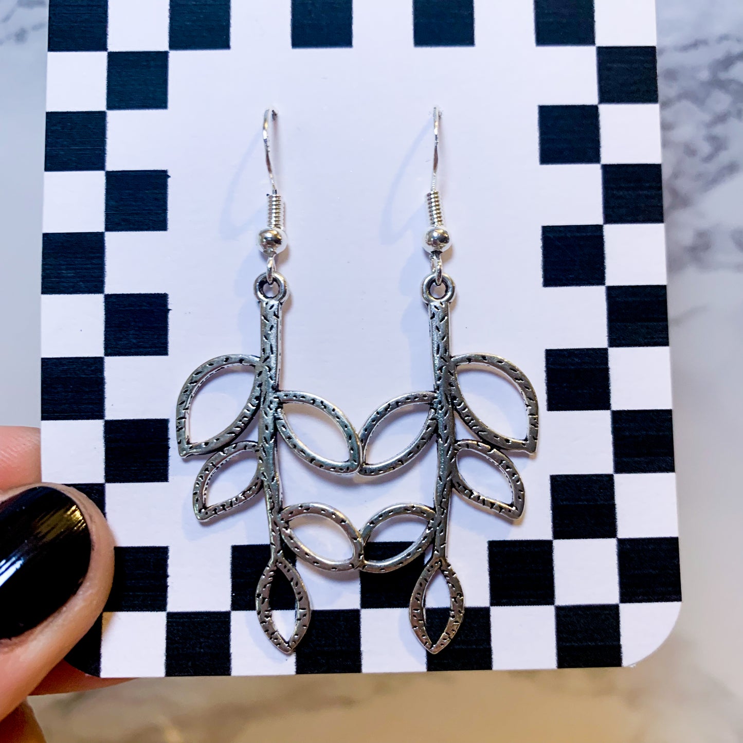 Silver leaf dangle earrings on a black and white checkered backing card with the title isymakesthings