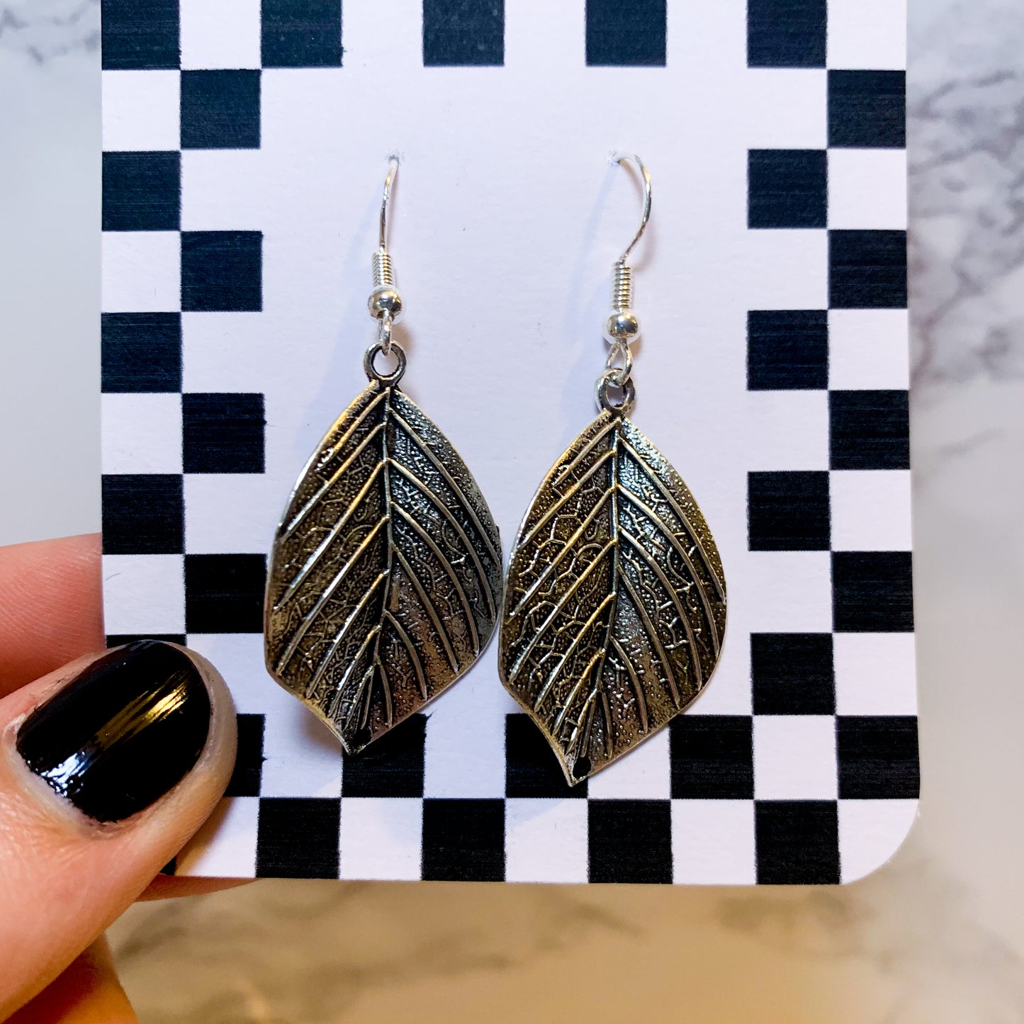 Silver leaf dangle earrings on a black and white checkered backing card with the title isymakesthings