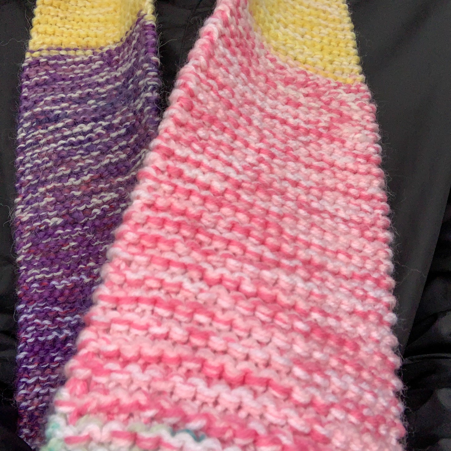 A close up of a green purple yellow and pink colour block knitted scarf showing the variegated pink knitted block