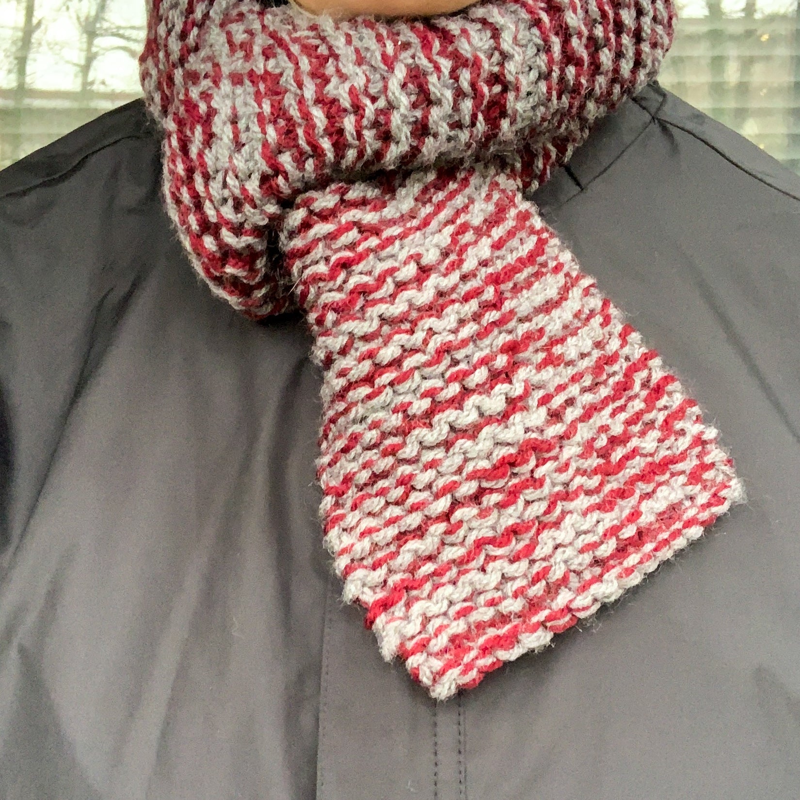 A burgundy and grey variegated scarf is looped through itself around a persons neck