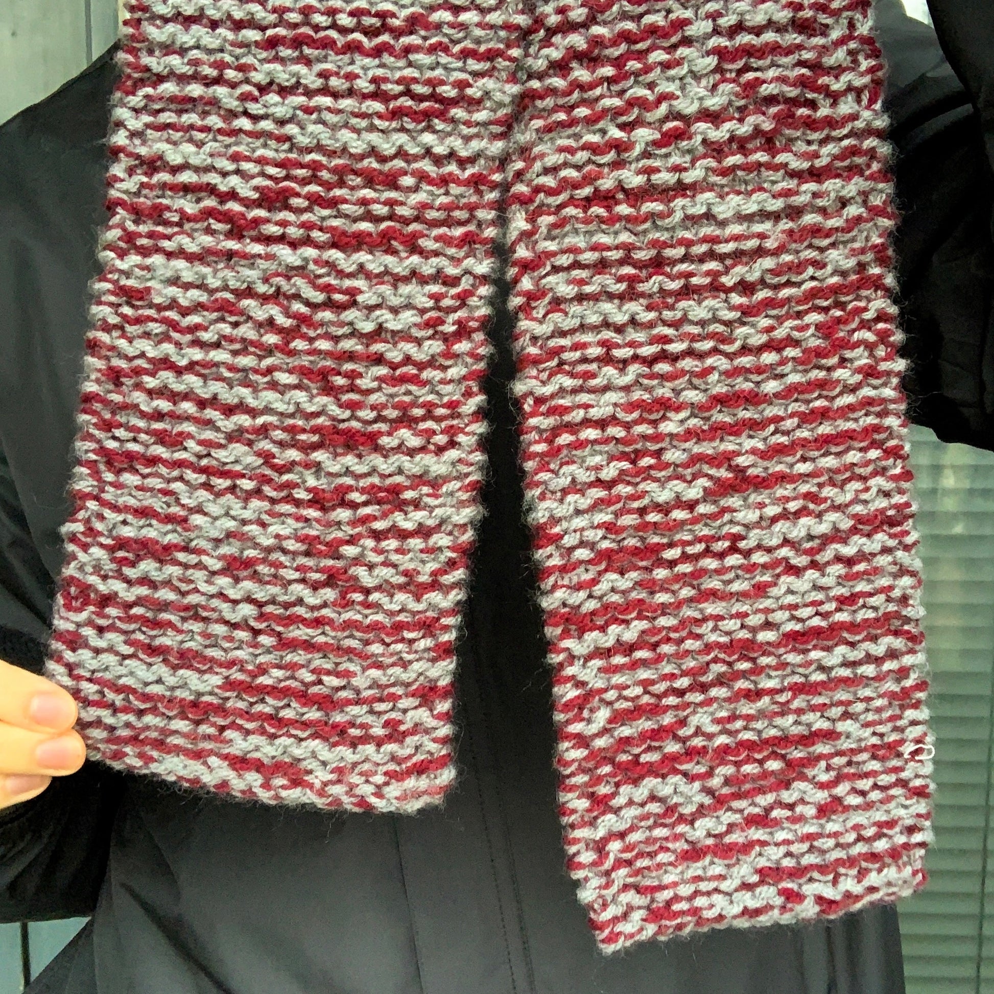 A burgundy and grey variegated scarf in held up a displayed by a person