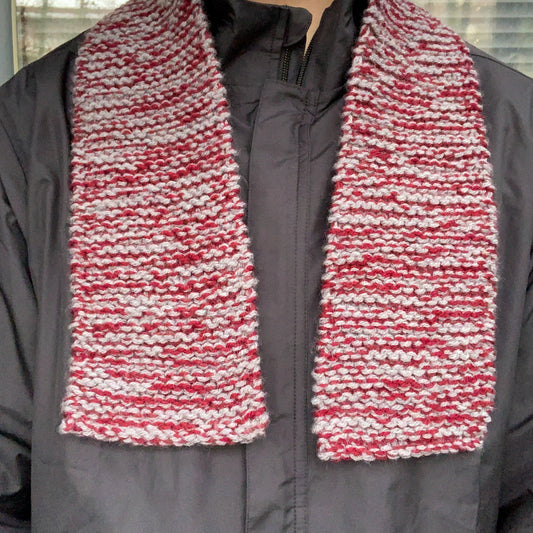 A burgundy and grey knitted scarf hangs off a persons shoulders