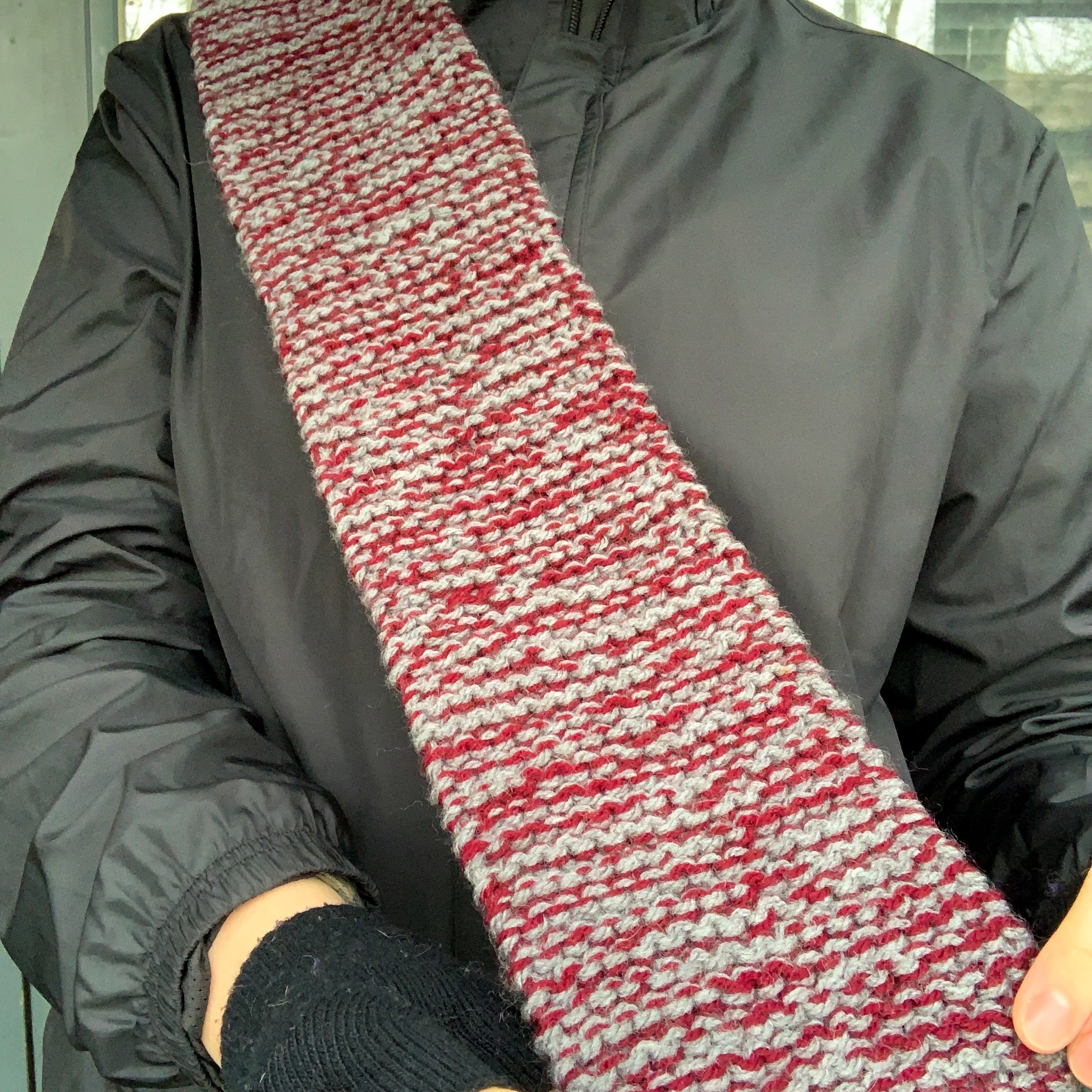 A burgundy and grey variegated scarf in held up a displayed by a person