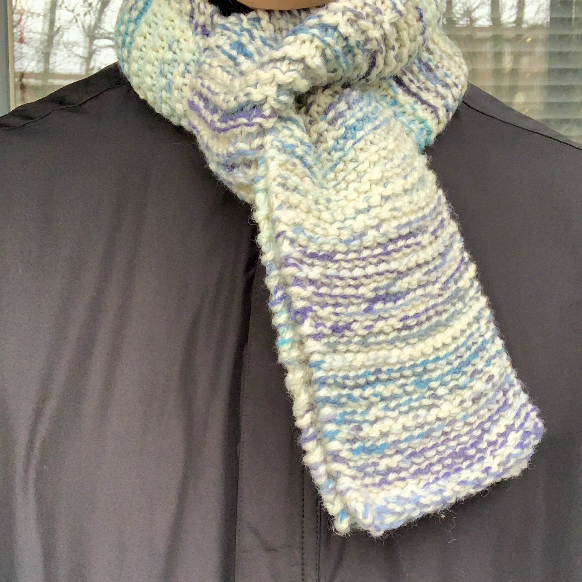 A blue & white variegated scarf is wrapped around someones neck and thread through itself 