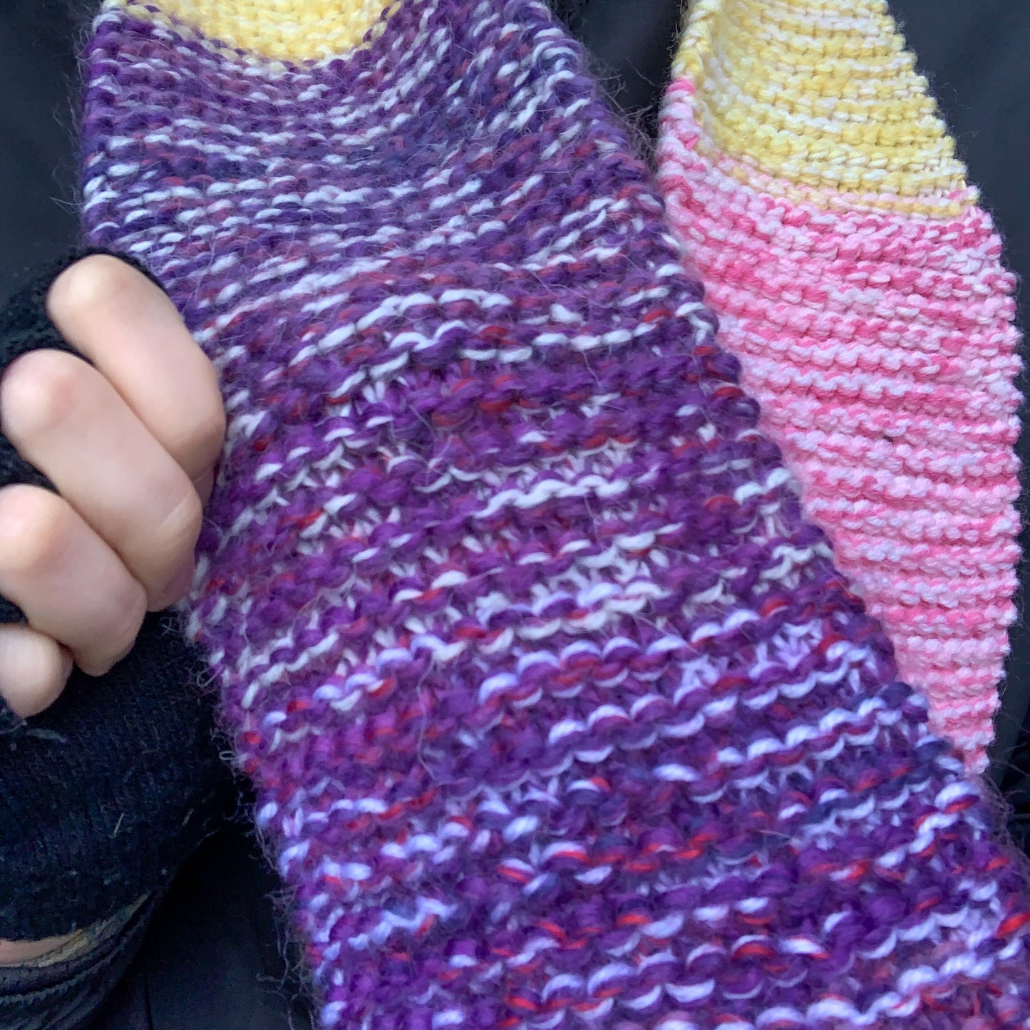 A close up of a green purple yellow and pink colour block knitted scarf showing the variegated purple knitted block