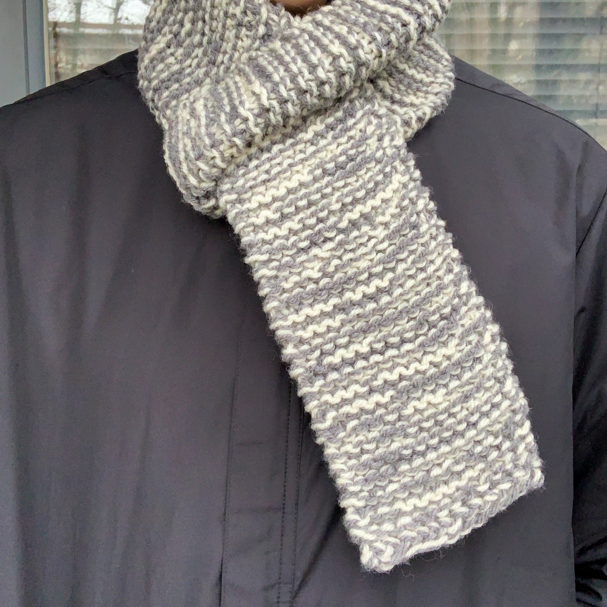 A grey & white variegated scarf is wrapped round a persons neck and tucked through itself