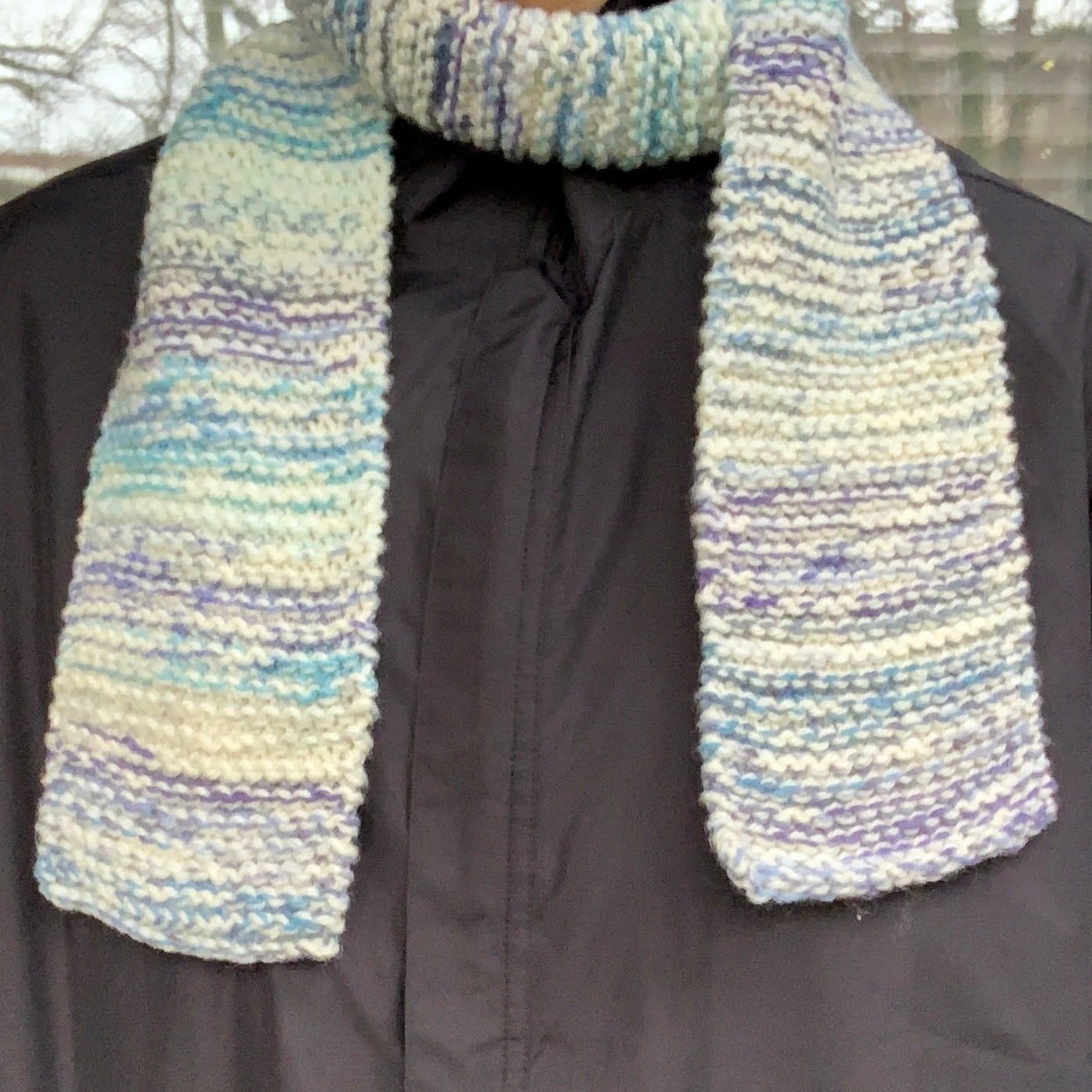 A blue & white gradient variegated scarf is wrapped round a persons neck with pieces dangling down their front on both sides