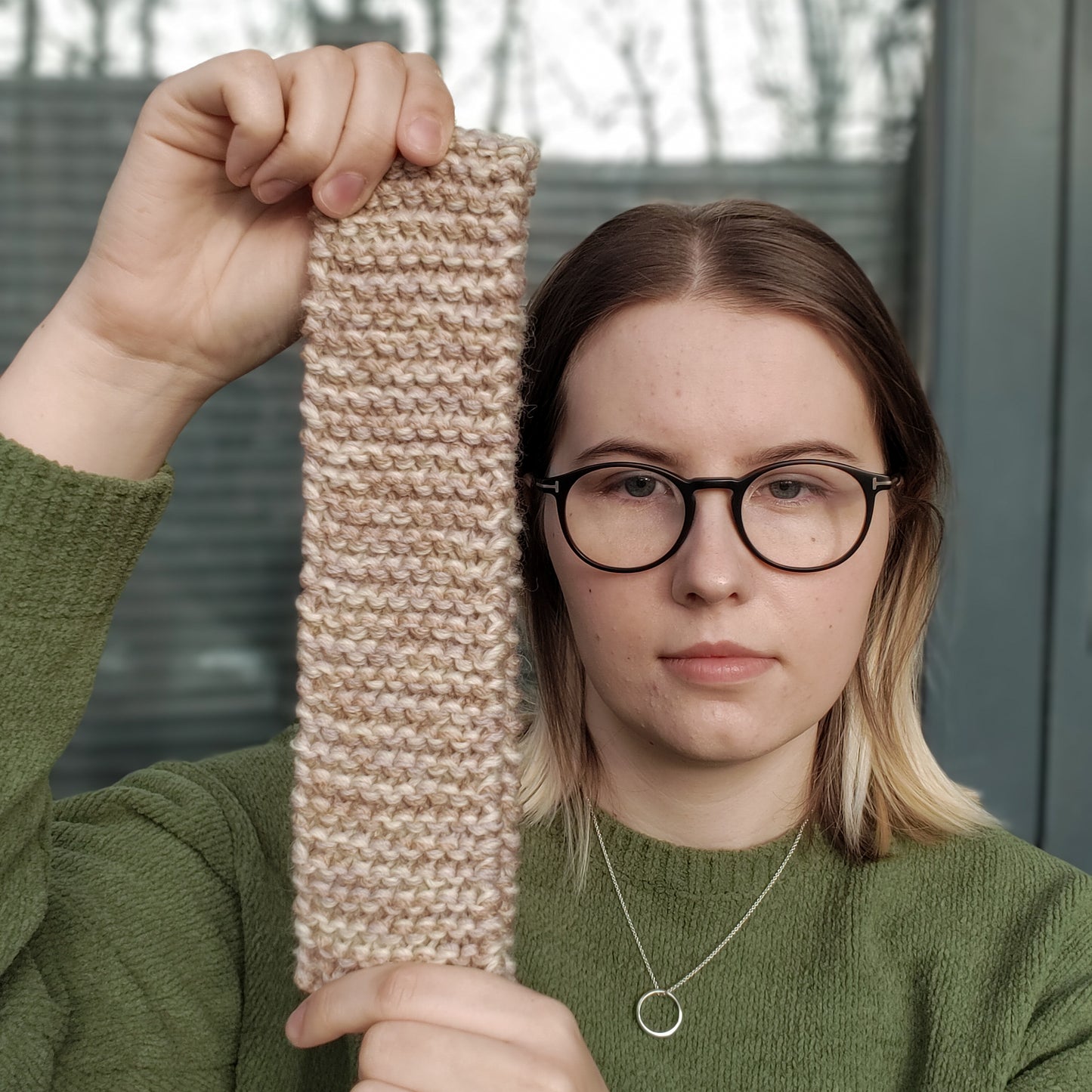 A woman holds up a beige variegated ear warmer knitted headband