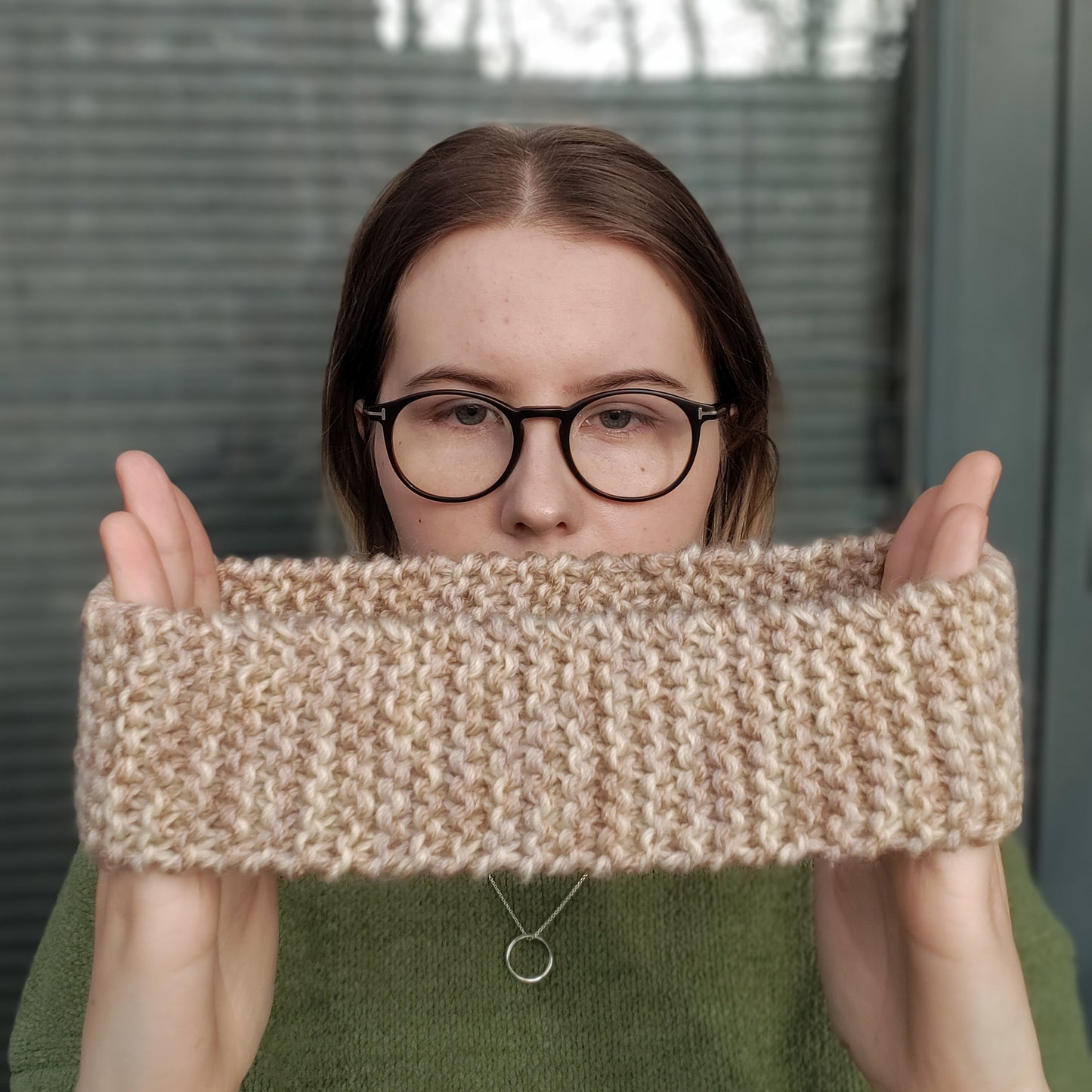 A woman holds a beige variegated ear warmer knitted headband between her hands